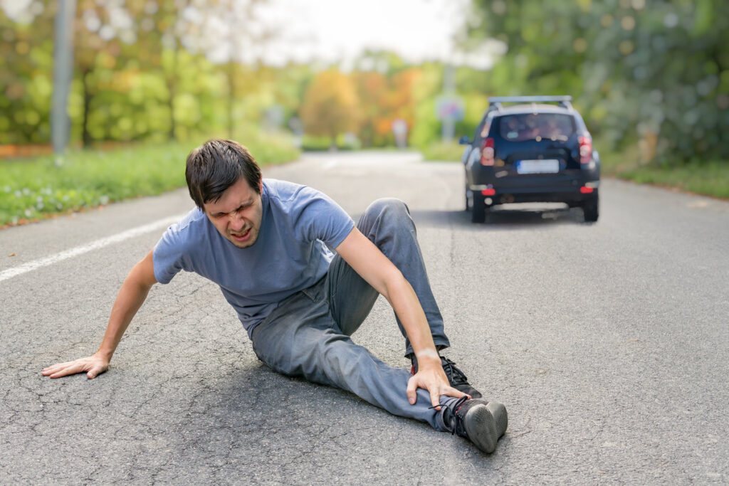 Hit and run concept. Injured man on road in front of a car.